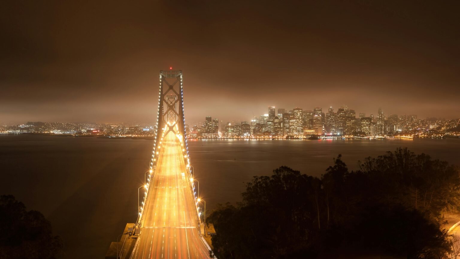 Aerial view of the Golden Gate Bridge leading to illuminated San Francisco skyline at night.